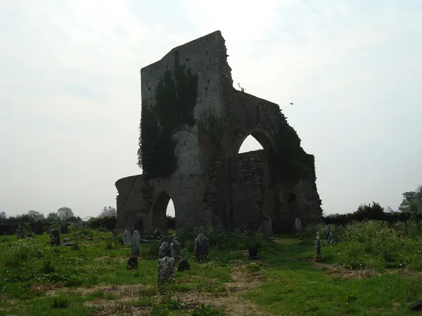 Eine hohe, verfallene Steinmauer der Abtei mit Bogenöffnungen, die auf einem grasbewachsenen Friedhof steht.