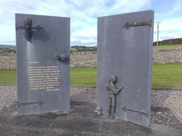 Two tall slate panels shaped like doors with a bronze figure of a boy between them and fields behind.