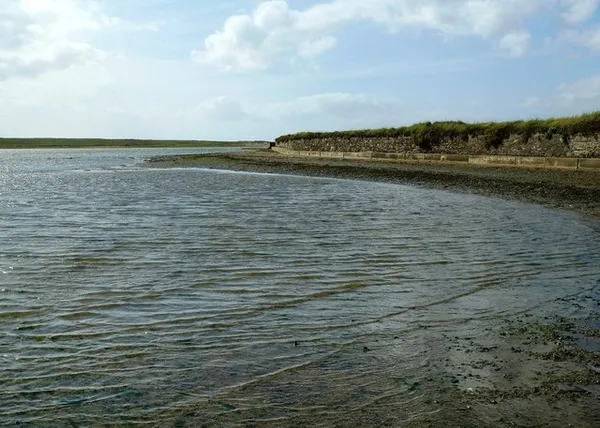 Calm lagoon water curving towards a low grassy bank beneath a pale sky.