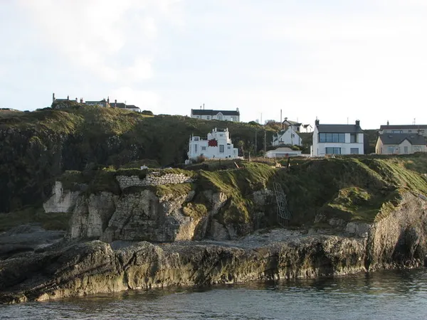 White houses on top of a grassy, rocky cliff above the sea.