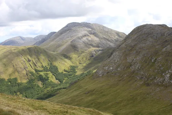 Grassy mountain slopes rising to a rounded peak above a green valley with a patch of forest.