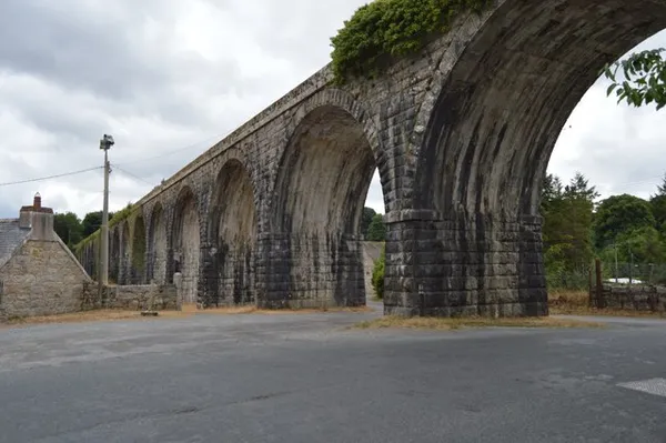 A tall stone railway viaduct with a row of arches stretching into the distance over a road.
