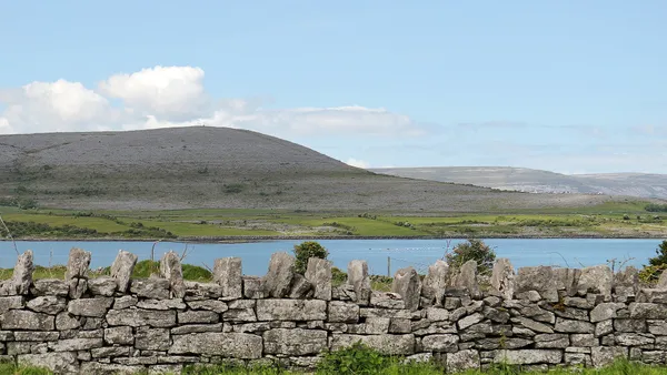 Une large colline de calcaire gris s'élevant au-delà d'une étendue d'eau, avec un mur de pierres sèches devant.