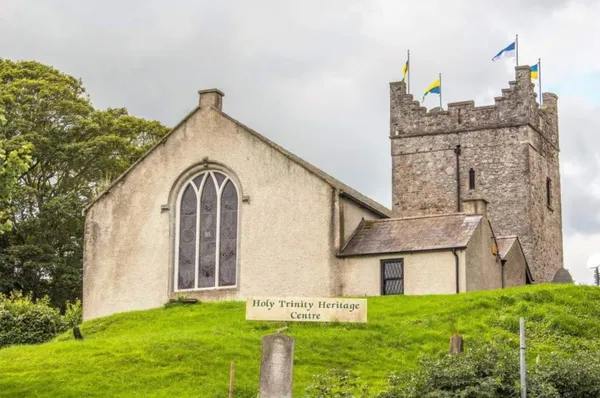A cream-rendered former church with an arched window beside a crenellated stone tower flying flags.