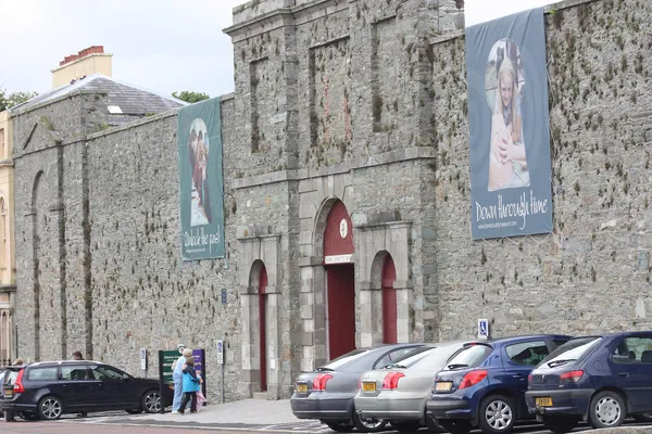 Stone gaol frontage with arched red doors and exhibition banners on the walls, cars parked in front.