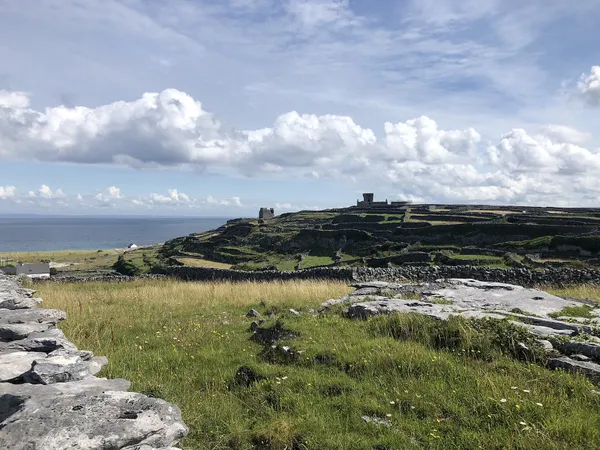 Limestone rocks and grass in the foreground lead to a ridge with a ruined stone tower and walls, sea to the left.