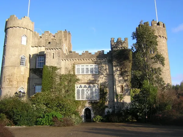 Ein steinernes Schloss mit runden Türmen und efeubewachsenen Mauern unter blauem Himmel.