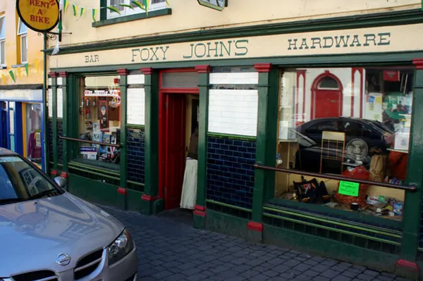 Grün gestrichene Ladenfront mit Schildern, die Bar, Foxy John's und Hardware lesen, und geflieste Fensterbänke.