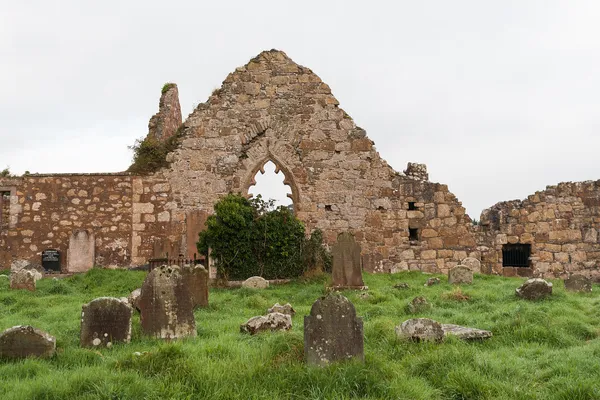A roofless stone church gable with a pointed window above a graveyard of old headstones.