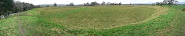 A panoramic view of a large circular grassy enclosure ringed by a raised earth bank.