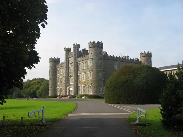 Castellated stone front of Gormanston Castle with towers, a lawn and a clipped yew.