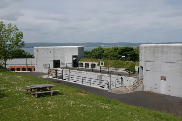 Concrete gun emplacements and a central bunker on a grassy slope, with a picnic table and the lough beyond.