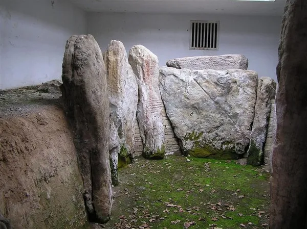 Tall weathered upright stones of a Neolithic burial chamber inside a protective enclosure.