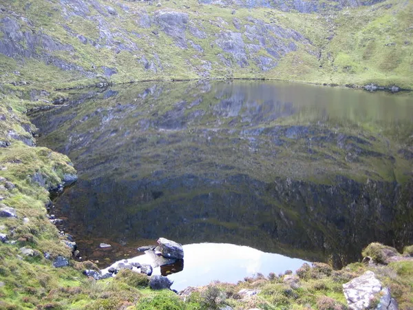 A mountain lake in a steep rocky hollow, with grassy cliffs mirrored in the calm water.