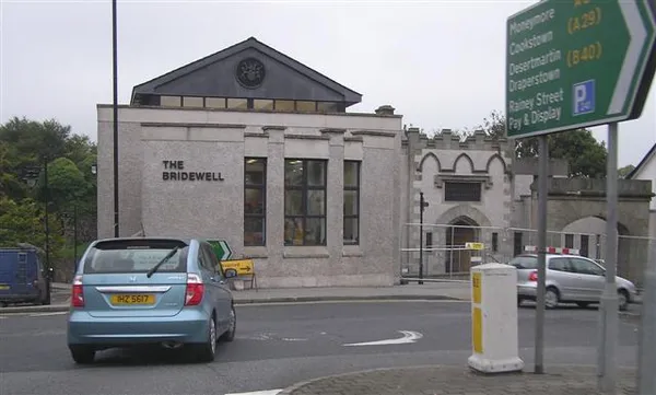 Stone front of the Bridewell building in Magherafelt with a road sign and passing car.