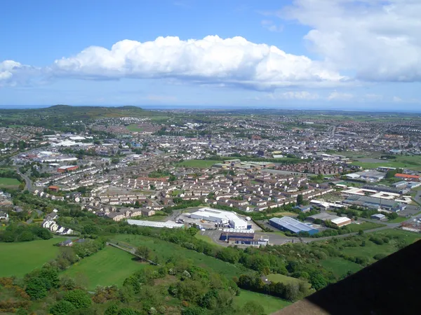 Une vue élevée sur une ville étendue de maisons et de bâtiments industriels parmi des champs verts sous des nuages blancs.