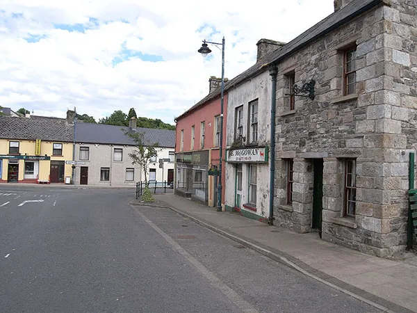A quiet village street lined with stone and painted terraced buildings under a partly cloudy sky.