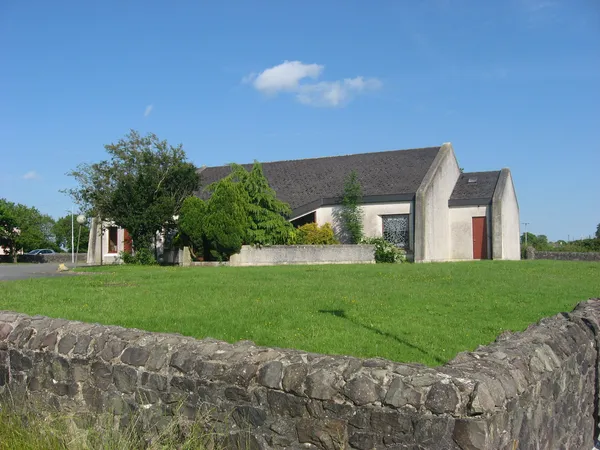 A modern church with a pitched roof behind a stone wall and lawn under a blue sky.