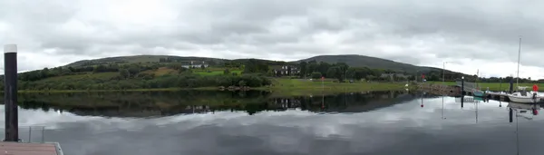 Une longue colline verte s'élevant au-delà d'un lac calme qui reflète le ciel gris nuageux.