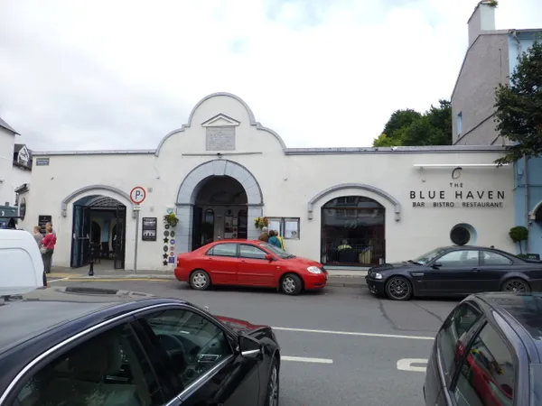 Un edificio bianco con archi e un'insegna Blue Haven, con auto parcheggiate in strada.