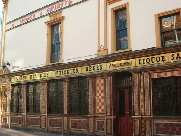 An ornate pub front with coloured tiles, carved wooden lettering and tall windows.