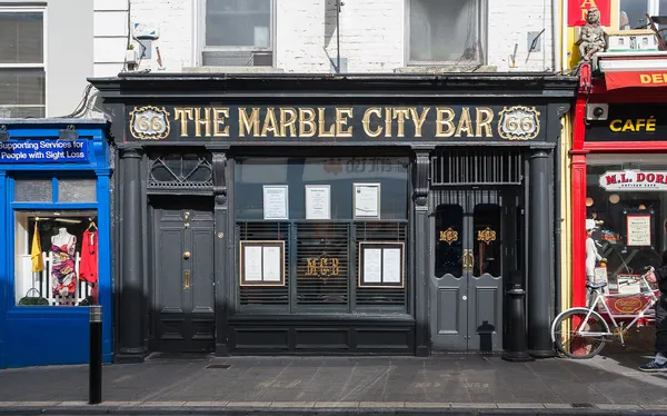 A dark painted pub front with gold lettering reading The Marble City Bar.